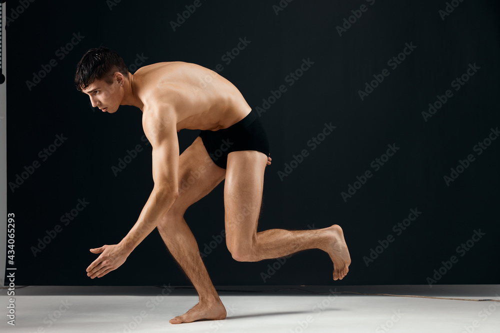 sporty man in black shorts with a muscular body on a dark background sporty man in black shorts with a muscular body on a dark background