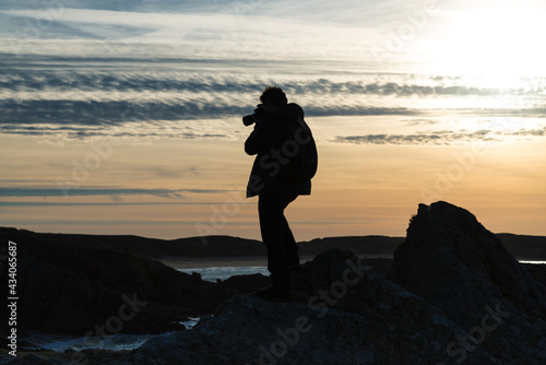 Silhouette of a photographer with a camera in his hands on a background of the sky at sunrise