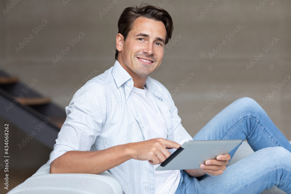 Handsome smiling man with digital tablet on the sofa at home, looking at the camera online shopping Handsome smiling man with digital tablet on the sofa at home, looking at the camera online shopping