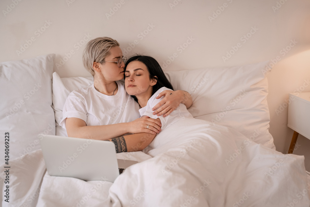 Fototapeta premium young lesbian couple hugging while lying on bed near laptop