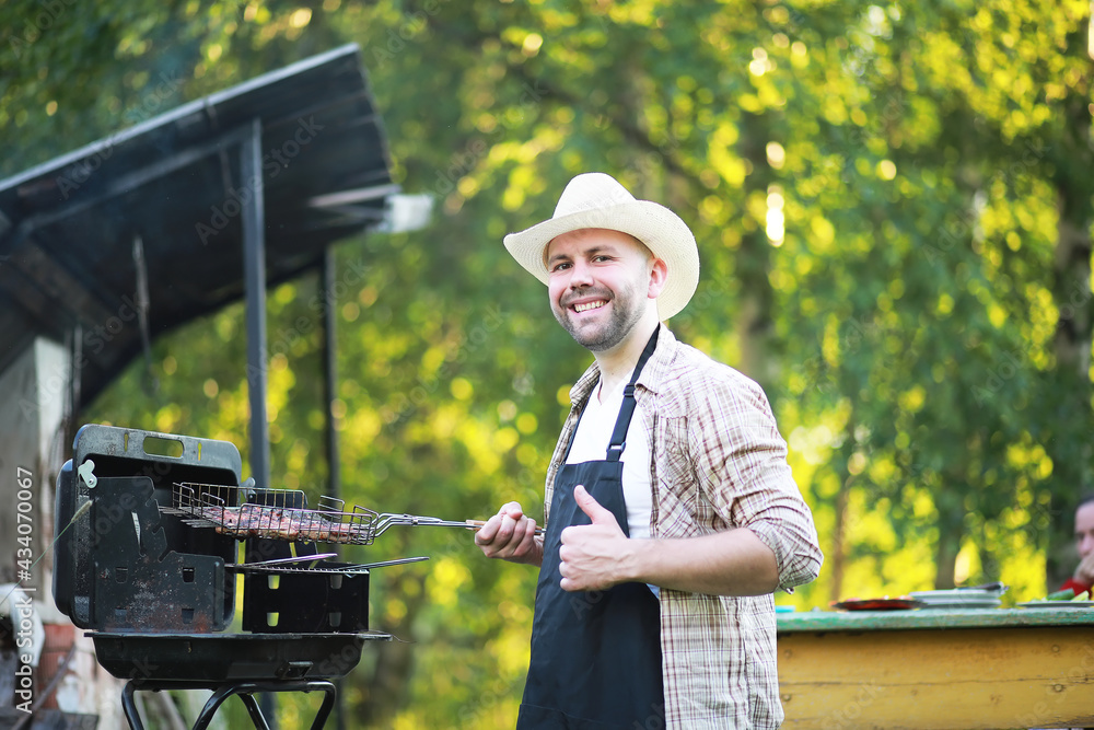 Barbecue time. European man in hat waiting for grilled food. He is sitting near fire and rest. Barbecue time. European man in hat waiting for grilled food. He is sitting near fire and rest.