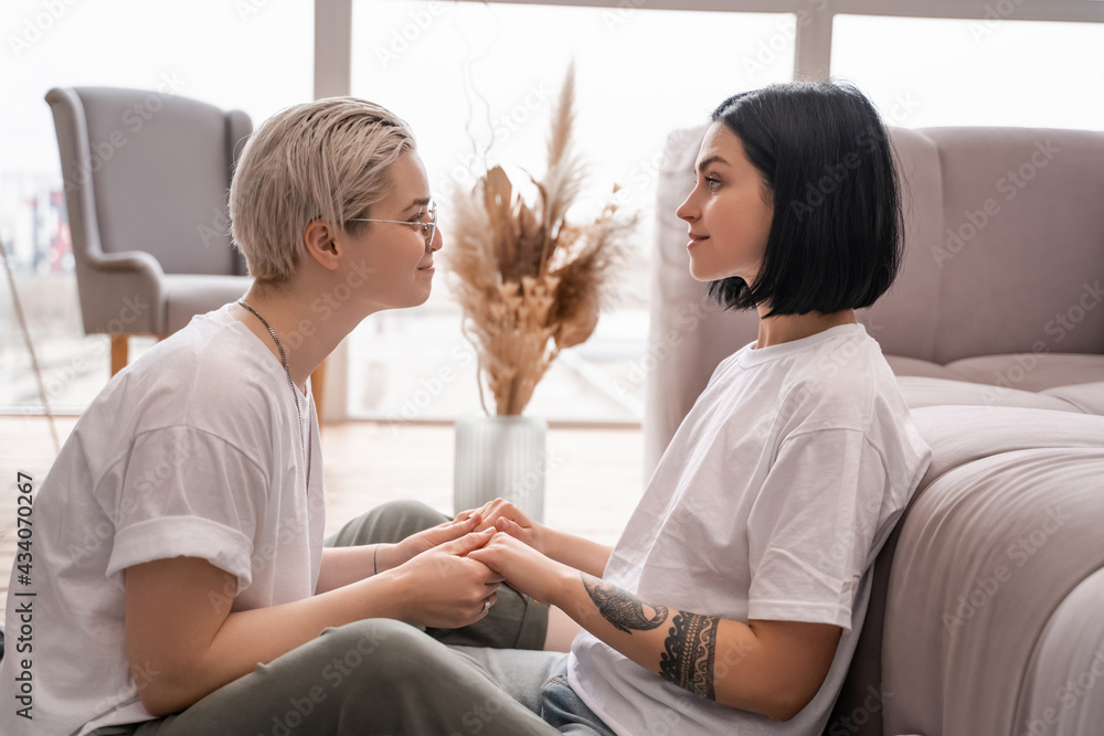 side view of cheerful lesbian couple holding hands in living room