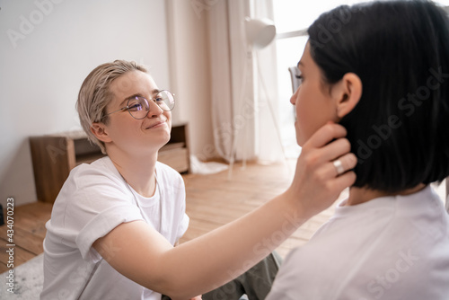 lesbian woman in glasses adjusting hair of girlfriend on blurred foreground