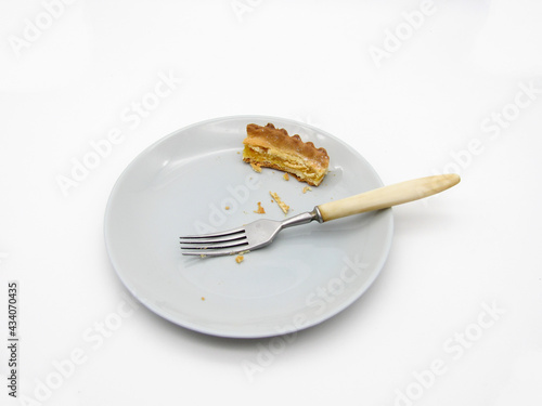 Leftovers from a piece of baked pie on a gray plate and a fork. Food stubs.