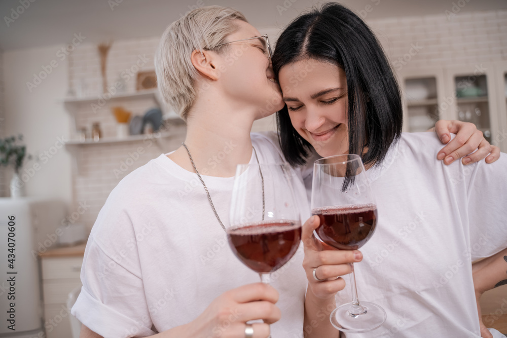 woman in glasses kissing happy girlfriend while holding glasses of red wine woman in glasses kissing happy girlfriend while holding glasses of red wine