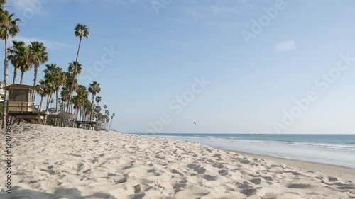 Tropical palm trees, white sandy beach by sea water wave, pacific ocean coast, San Clemente California USA. Blue sky and lifeguard tower. Life guard watchtower hut, summertime shore. Los Angeles vibes
