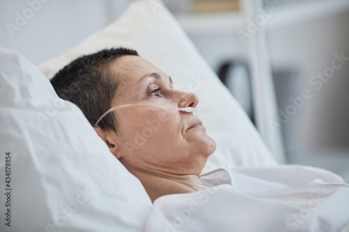 Side view of mature woman lying on hospital bed under dropper
