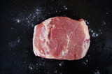 Raw piece of pork with salt on black background. Top view of Salted Piece of fresh boneless pork, neck part or collar. Big piece of red raw meat on a black background. Healthy lifestyle.