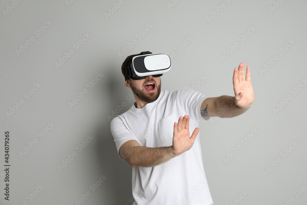 Emotional man using virtual reality headset on light grey background