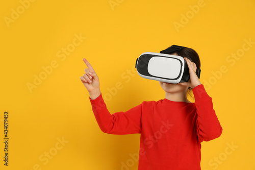 Little girl using virtual reality headset on yellow background