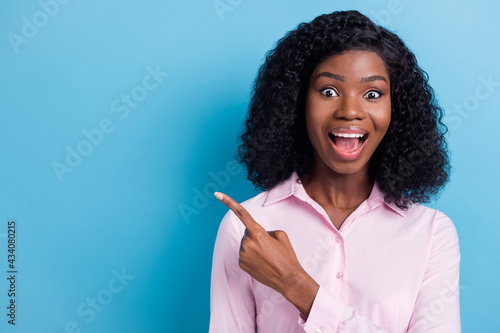Photo of funny impressed dark skin lady dressed pink clothes pointing finger empty space isolated blue color background