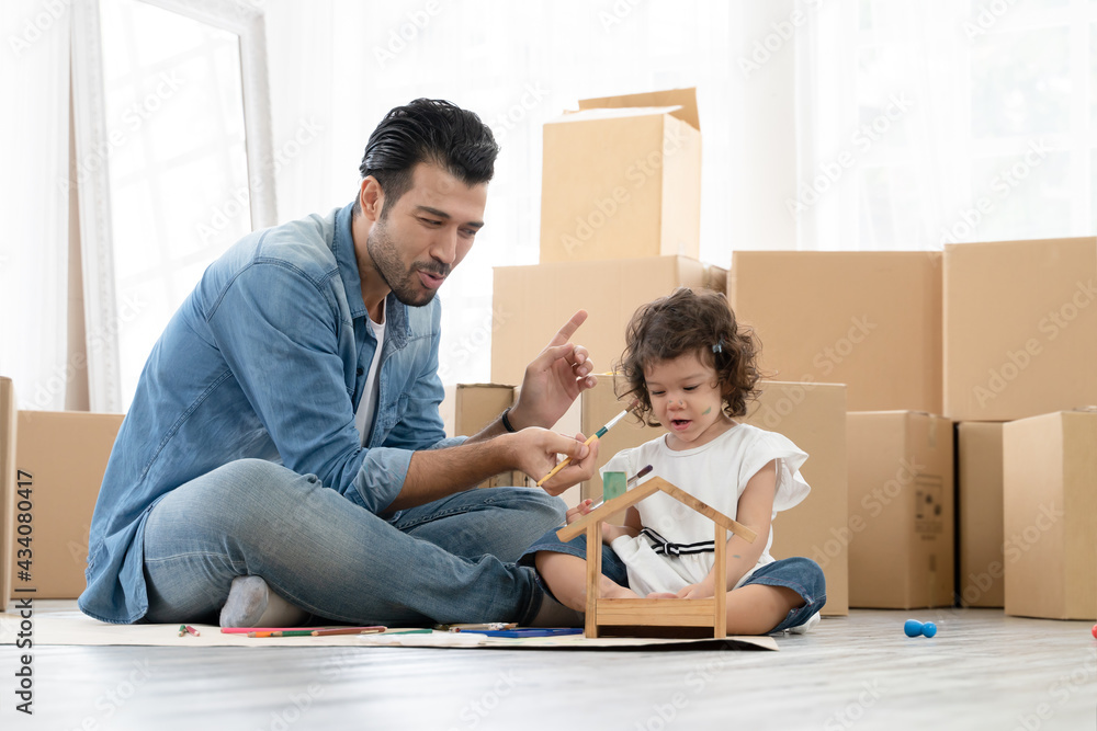Happy Caucasian young father and little daughter enjoy coloring wooden toy house together on new home floor. Dad tease cute child by putting a paint brush and paint water color on child's face. Happy Caucasian young father and little daughter enjoy coloring wooden toy house together on new home floor. Dad tease cute child by putting a paint brush and paint water color on child's face.