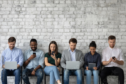 Multicultural team of gadget users sitting in line, using laptops, tablets, mobile phones, working, reading messages, chatting online on social media, watching content on internet. Copy space photo