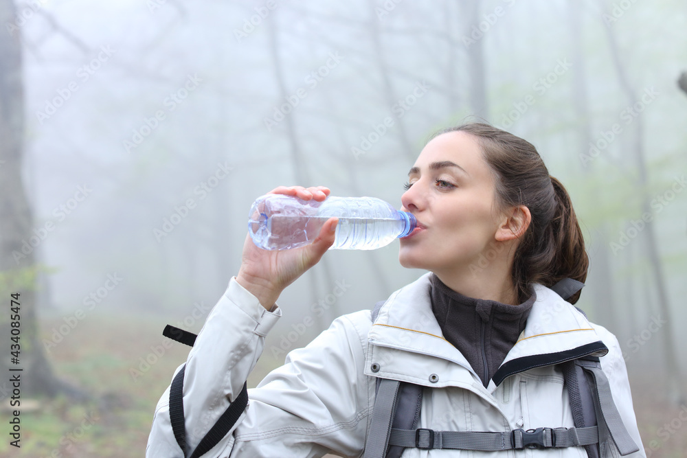 Hiker drinking water from plastic bottle in a forest Hiker drinking water from plastic bottle in a forest