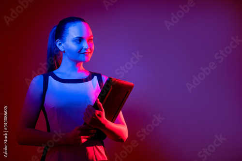 Digital lifestyle. Futuristic technology. Virtual business. Curious smart confident woman with laptop in pink blue fluorescent neon light isolated on purple empty space background.