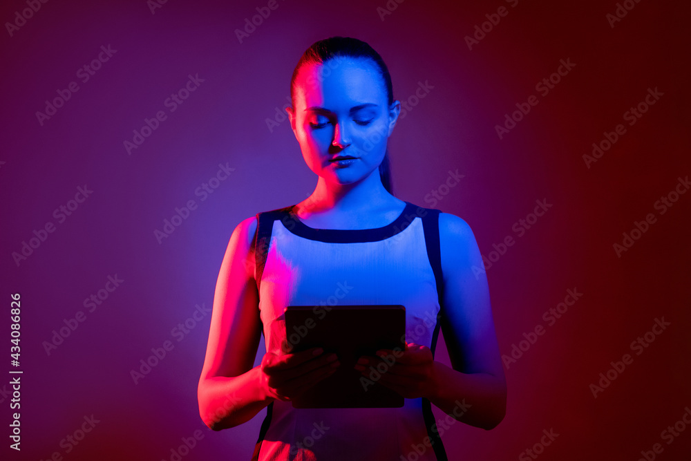 Cyber communication. ICT network. Futuristic technology. Smart neon light woman using tablet in pink blue fluorescent glow isolated on purple red empty space background. Cyber communication. ICT network. Futuristic technology. Smart neon light woman using tablet in pink blue fluorescent glow isolated on purple red empty space background.