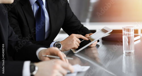 Businessman using tablet computer and work together with his colleague in sunny modern office, close-up. Unknown business people at meeting. Teamwork and partnership concept