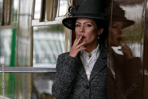 Fotografie Beautiful female in vintage 1920s costume smoking cigarette while leaving train