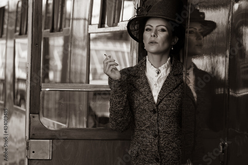 фотографія Beautiful female in vintage 1920s costume smoking cigarette while leaving train