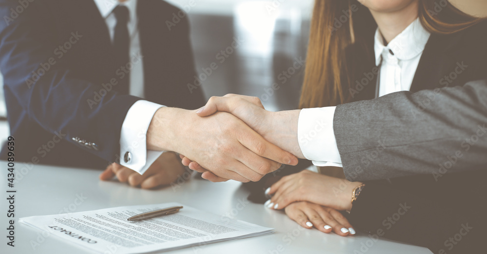 Unknown businessman shaking hands with his colleague or partner above the glass desk in modern office, close-up. Business people group at meeting Unknown businessman shaking hands with his colleague or partner above the glass desk in modern office, close-up. Business people group at meeting