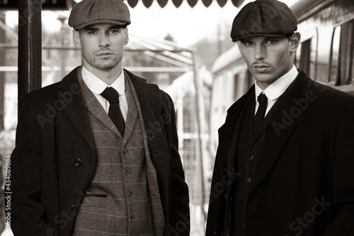 Handsome English gangsters smoking at railway station with train in the background photo