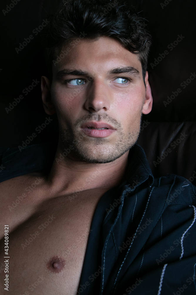 Portrait of attractive young man with stubble and open shirt revealing defined pecs, sitting in leather armchair Portrait of attractive young man with stubble and open shirt revealing defined pecs, sitting in leather armchair