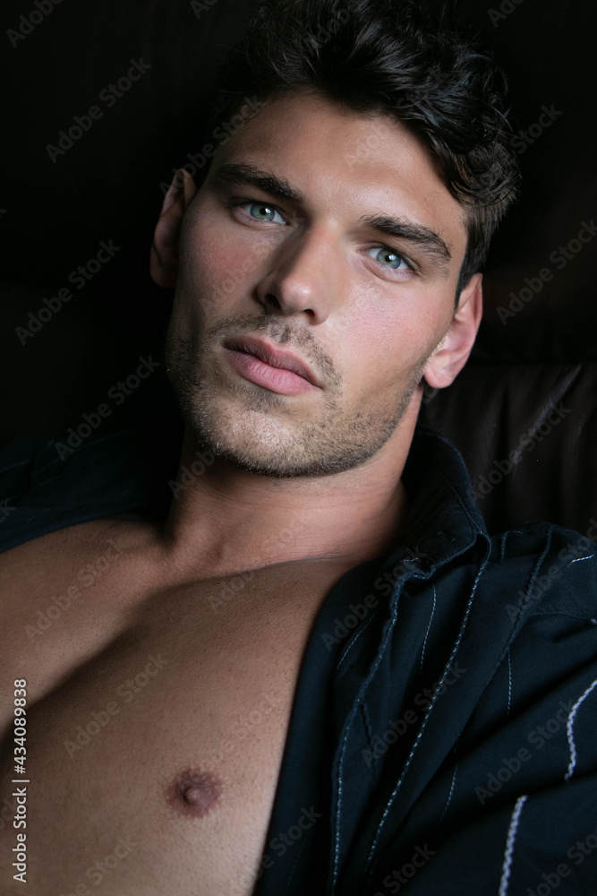 Portrait of attractive young man with stubble and open shirt revealing defined pecs, sitting in leather armchair Portrait of attractive young man with stubble and open shirt revealing defined pecs, sitting in leather armchair