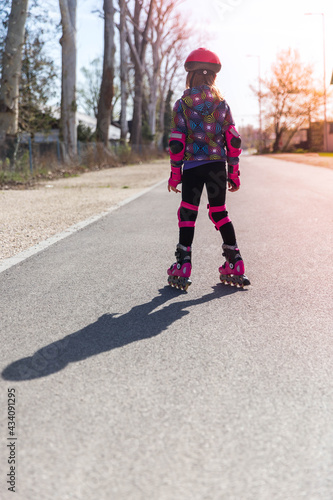 Little girl in pink roller skates and protective equipment outdoors on the road