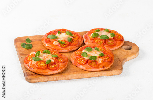 Small open pies pizzas with beet juice added to the dough, with cherry tomatoes, mozzarella and basil on a wooden board on a white background