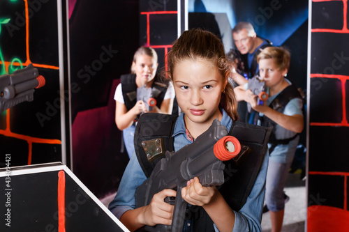 Emotional teen girl with a laser pistol playing laser tag with family on a dark labyrinth
