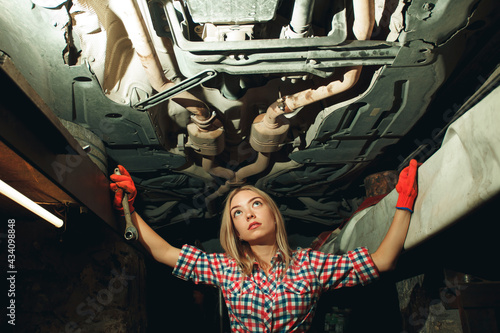 Handsome mechanic in uniform are working in auto service with lifted vehicle. Car repair and maintenance. Mechanic examining under the car at the repair garage.