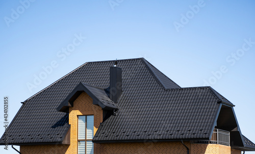 Brown corrugated metal profile roof installed on a modern house with a attic windows. The roof of corrugated sheet. Roofing of metal profile wavy shape. Modern roof made of metal. Metal roofing. © Volodymyr