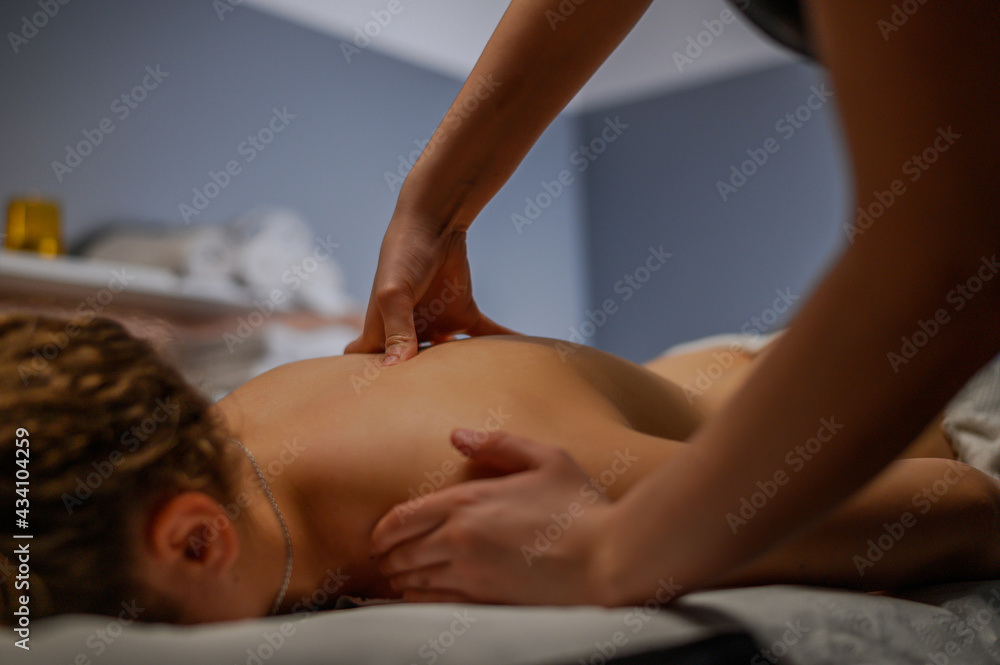 Obraz premium Masseur hands massaging back and shoulder blades of female lying on massage table