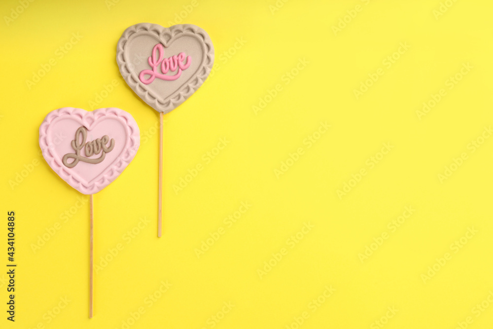 Chocolate heart shaped lollipops with word Love on yellow background, flat lay. Space for text