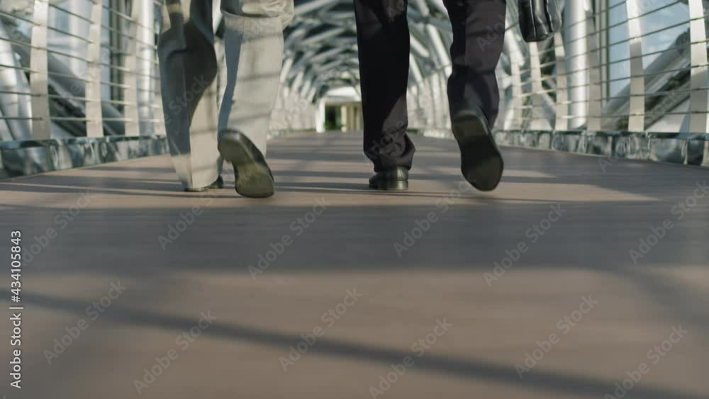 Low-section slowmo of unrecognizable businessmen legs walking along indoor glass walkway of modern high-class office building Low-section slowmo of unrecognizable businessmen legs walking along indoor glass walkway of modern high-class office building