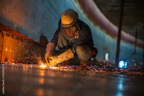 Male worker metal cutting spark on tank bottom steel plate with flash of cutting light close up wear protective gloves and mask