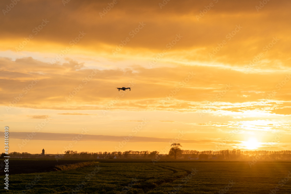 drone flying over green springtime meadows with a colorful orange sunset sky behind