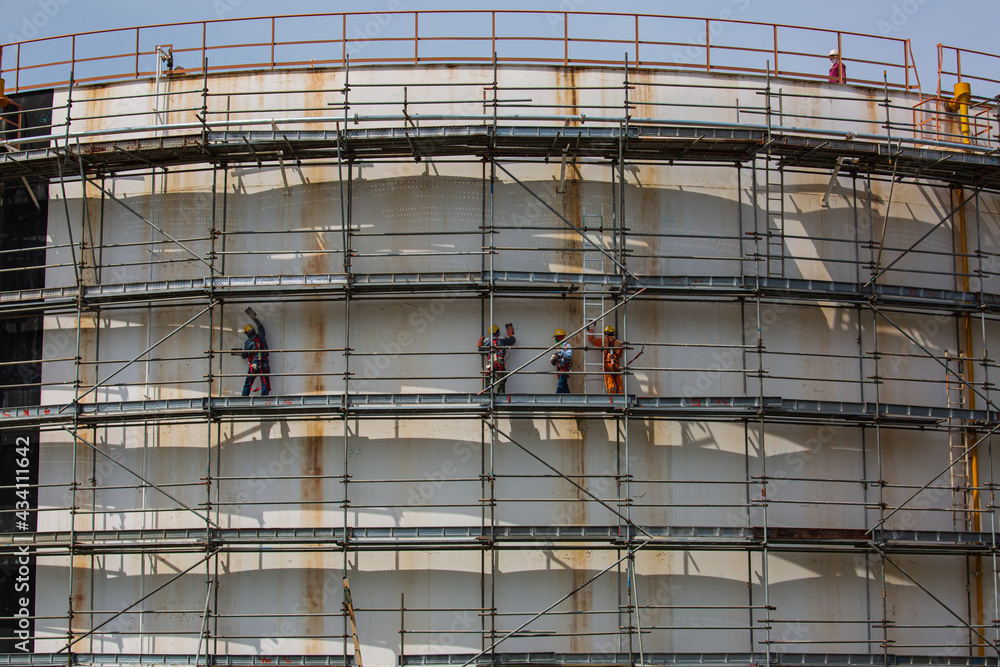 Construction workers tank oil installing scaffolding