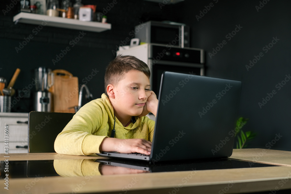 Boy in yellow clothes is watching movie, studying or playing game online on computer at home kitchen background and smiling Boy in yellow clothes is watching movie, studying or playing game online on computer at home kitchen background and smiling