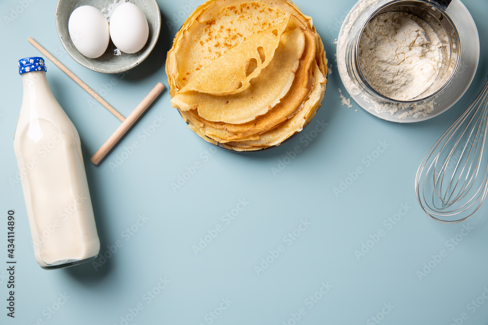 Stack of homemade crepes and ingredients for making thin pancakes around on blue background. Top view, copy space. Stack of homemade crepes and ingredients for making thin pancakes around on blue background. Top view, copy space.
