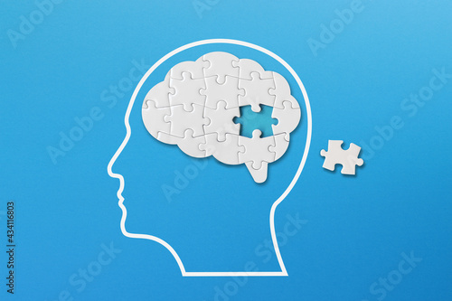 Brain shaped white jigsaw puzzle on blue background, a missing piece of the brain puzzle, mental health and problems with memory photo