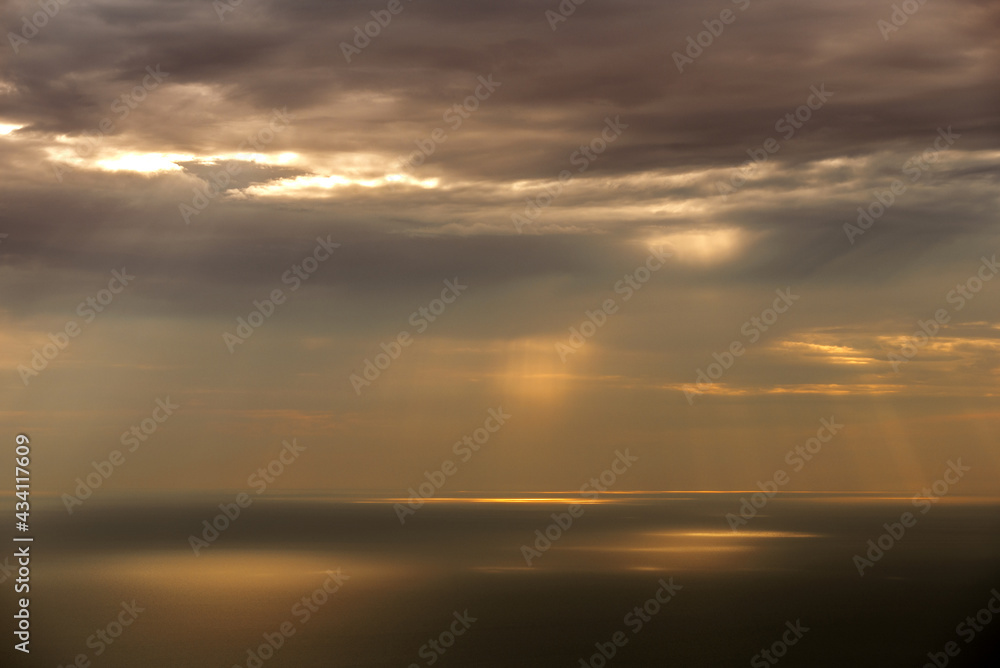 Sun rays shining through clouds on sea surface
