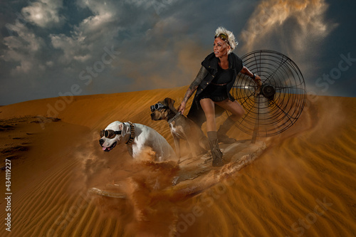 Post-apocalyptic woman is riding surfboard with big motor fan in Mad Max style with her Dogo Argentino and Pit Bull dogs on desert in smoke and dead wasteland on the background.