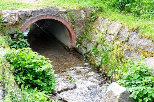 close-up concrete semicircular arch of a water drain well  a stream flows into a canal  sewage drains  the concept of a drainage system in Europe  a river drainage