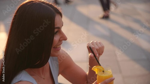 Smiling young woman drinks orange juice  at sunset outdoor photo