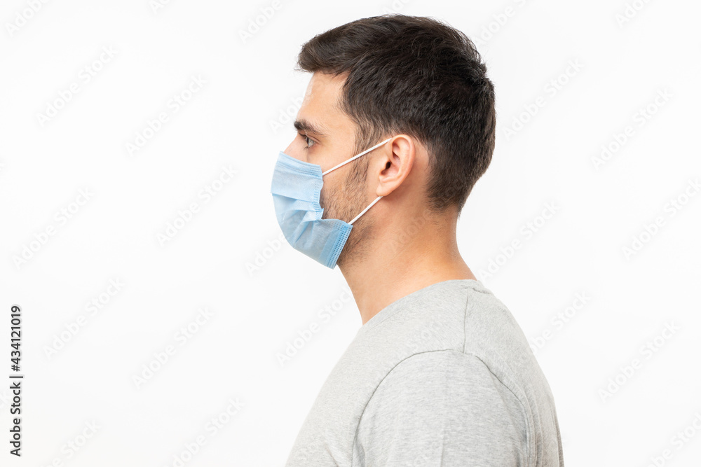 Left side view portrait of young man wearing casual t-shirt and face mask, isolated on gray background Left side view portrait of young man wearing casual t-shirt and face mask, isolated on gray background