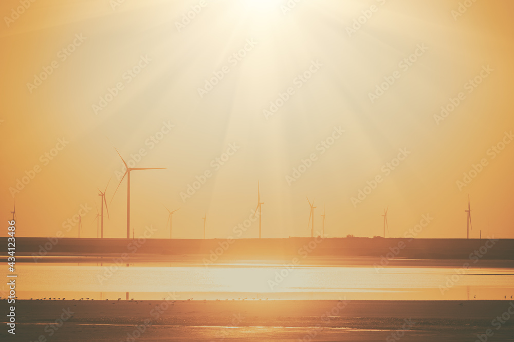 Wind farm and the salted lake Syvash at sunset, scenic industrial landscape in yellow tones with wind turbines, sky, sun beam and reflection in the water, Kherson oblast, Ukraine