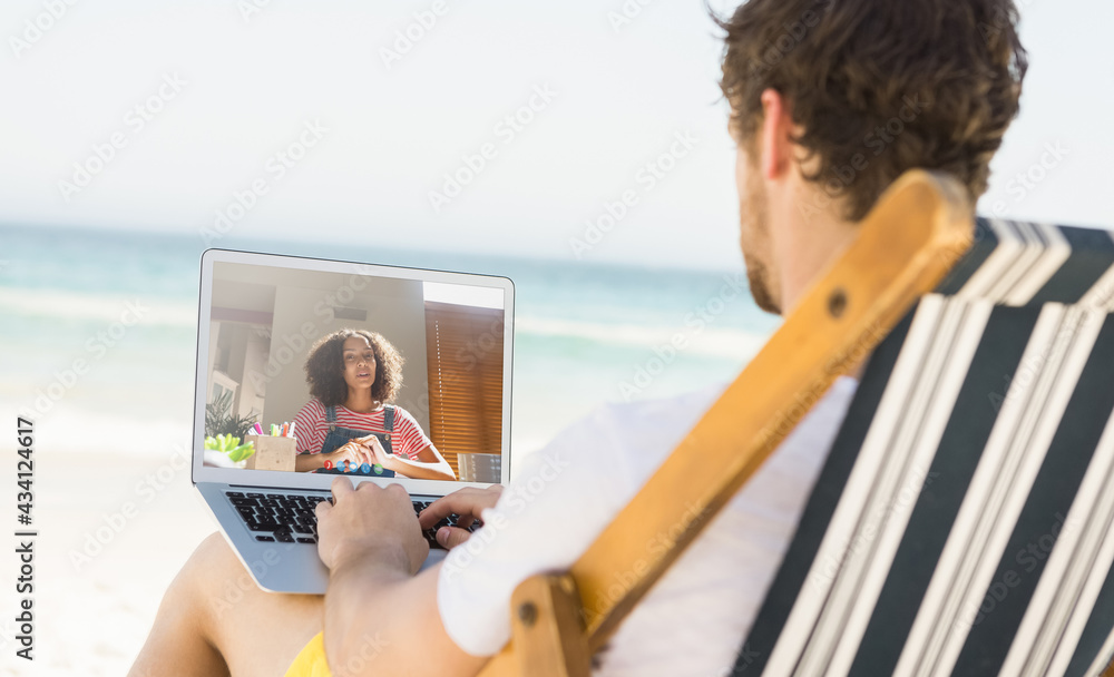 Caucasian man relaxing on beach having video call using laptop