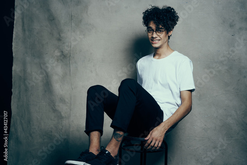 curly-haired guy sitting on a chair with glasses fashion studio © SHOTPRIME STUDIO