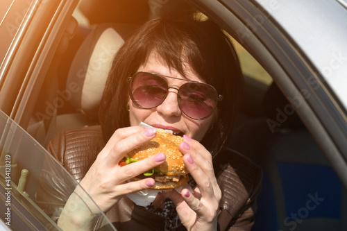 Happy young woman having lunch in the car. Sunglasses